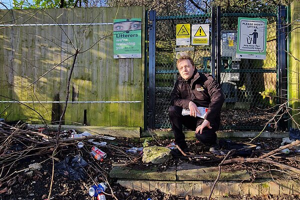 Councillor Charlie Clinton in front of a sign that says "Litterers, we're watching you", with a whole bunch of dumped litter
