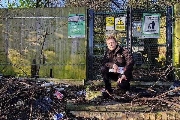 Councillor Charlie Clinton in front of a sign that says "Litterers, we're watching you", with a whole bunch of dumped litter
